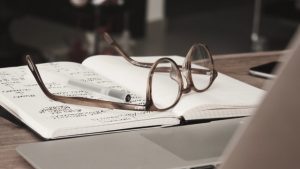 A pair of glasses and a pen on an open notebook.