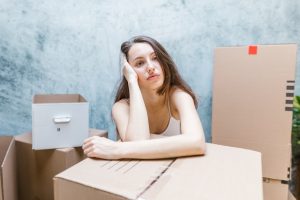 A woman surrounded with cardboard boxes feeling stressed out due to the upcoming relocation